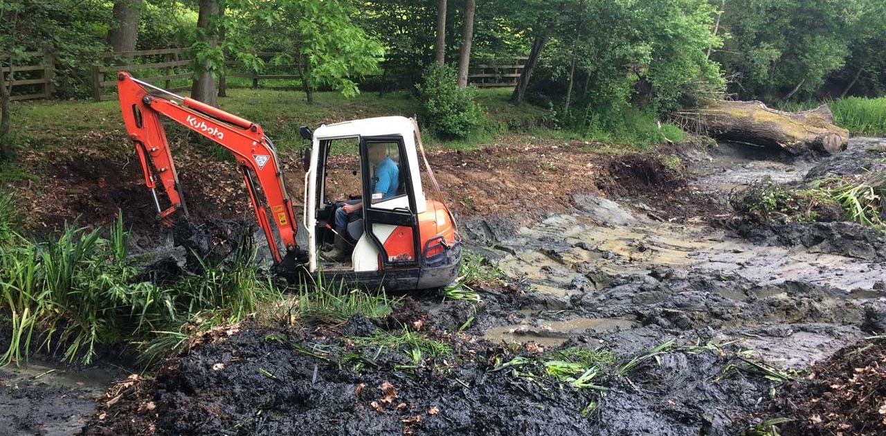 Image of a Kubota excavator clearing the side of a lake and preparing the ground works ready for traditional clay lake relining at Barkham in Berkshire - Let the digger do it!